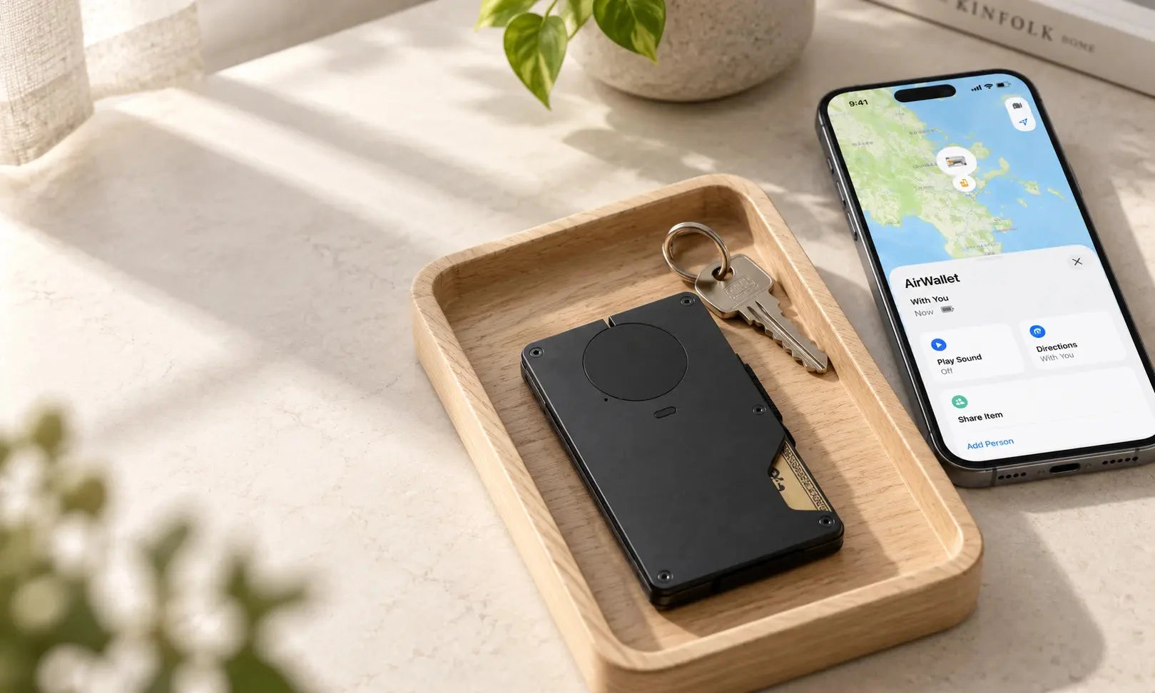 Black tracker wallet and keys in a wooden tray beside a phone displaying a location map.
